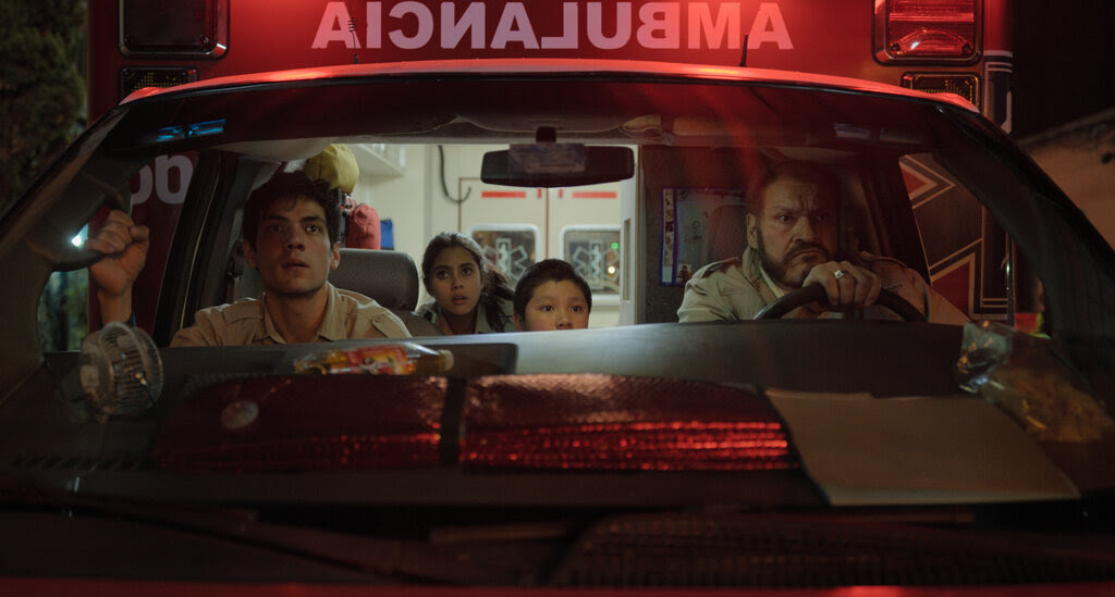 A man drives an ambulance, with three passengers, all staring out the windshield. 