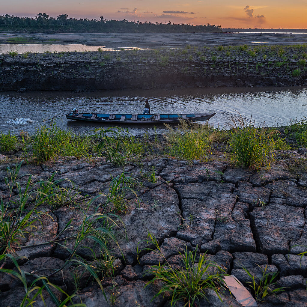 A person stands next to a canoe in shallow water. 