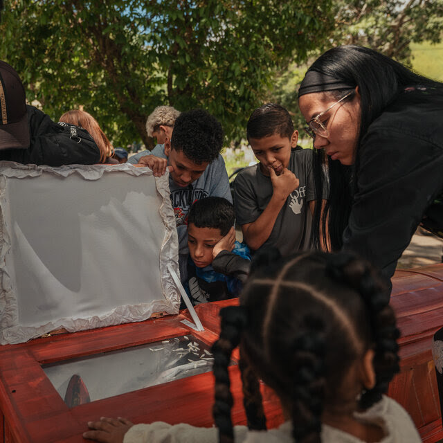 People standing over a coffin with a viewing window. 