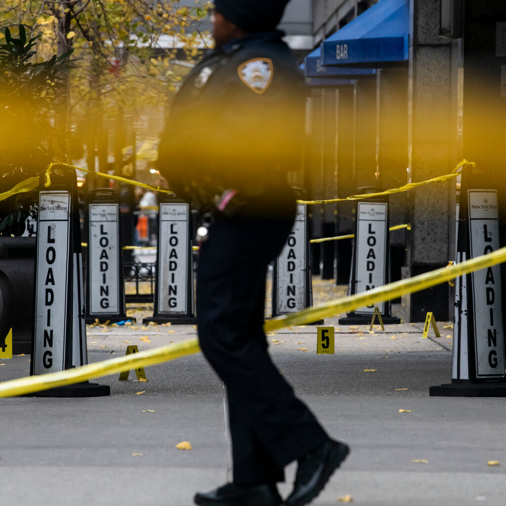 A police offer walks in between yellow cordon tape. 