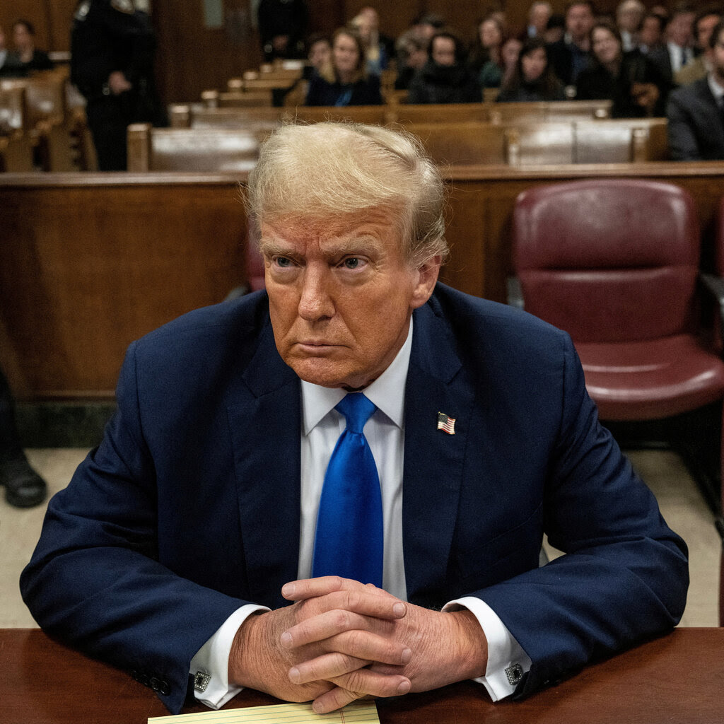 Donald Trump seated in a courtroom, wearing a blue jacket, white shirt and blue tie. 