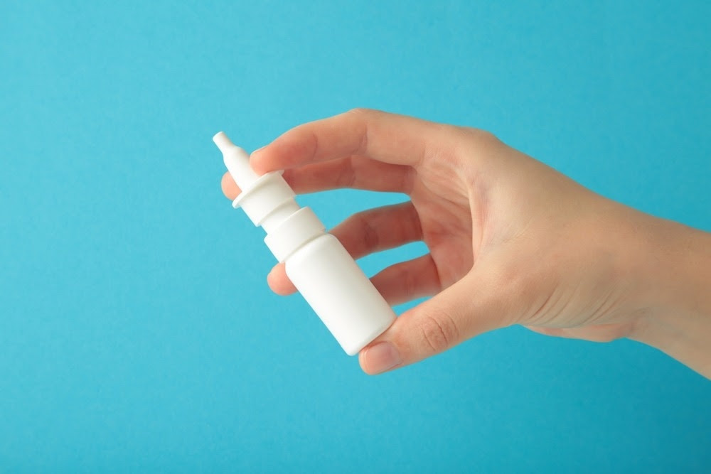 Hand holds a bottle of nasal spray on blue background.