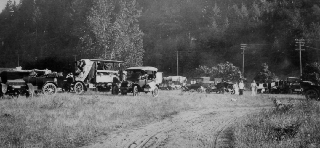 historic photograph of several early 20th century cars in a field with trees in the background