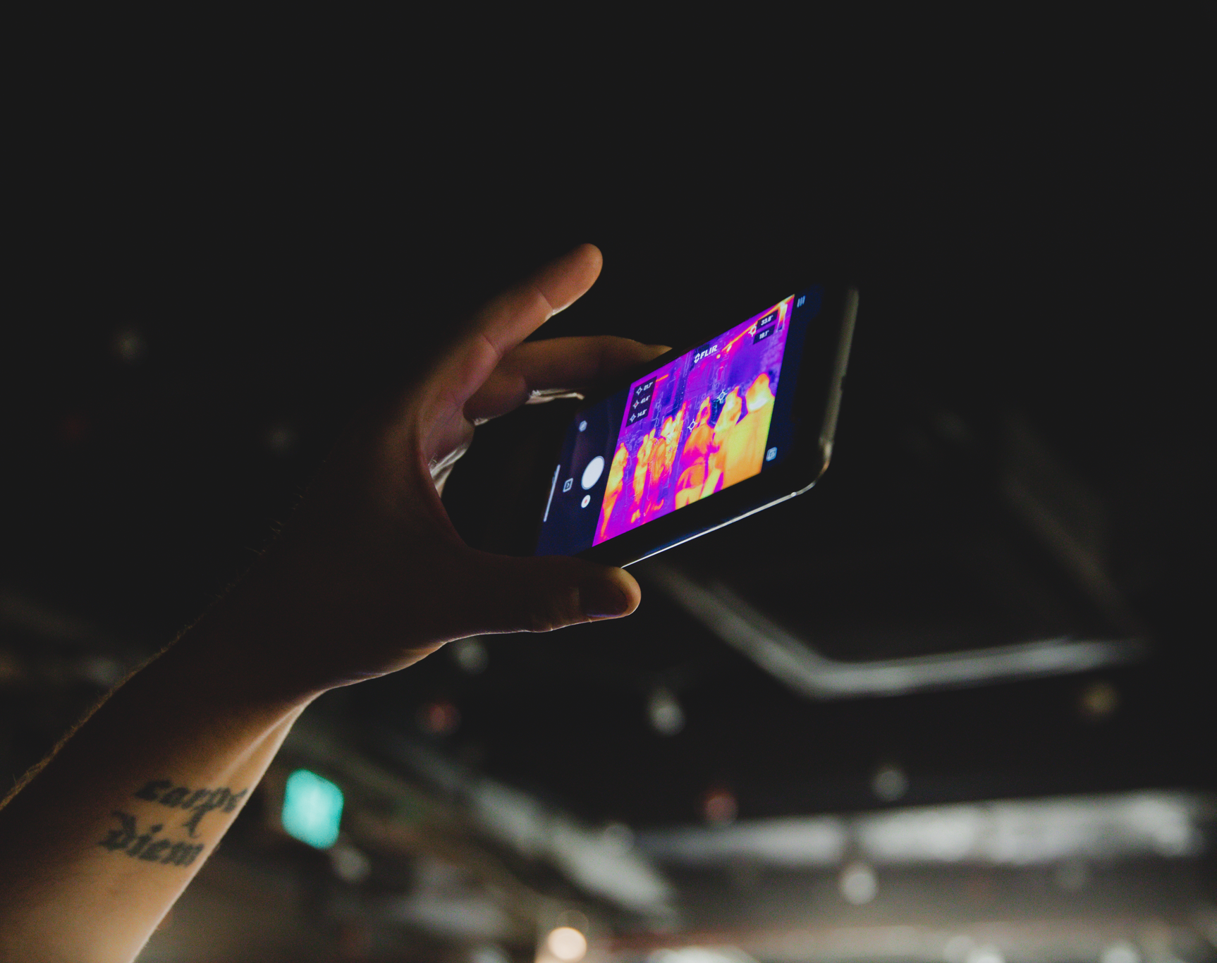 A hand holding up a phone displaying thermal imaging of a group of people.