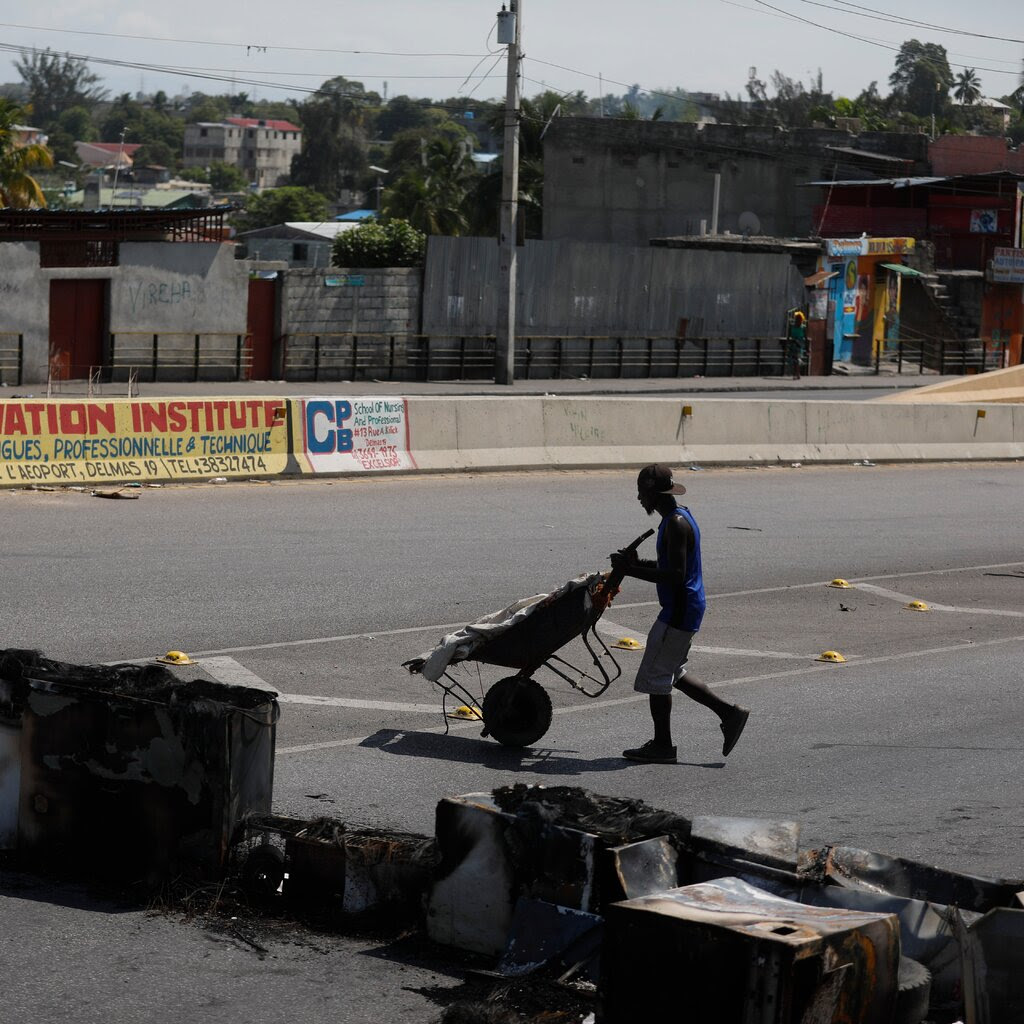 A man pushes a wheelbarrow past a makeshift roadblock set up by gangs in Port-au-Prince, Haiti.