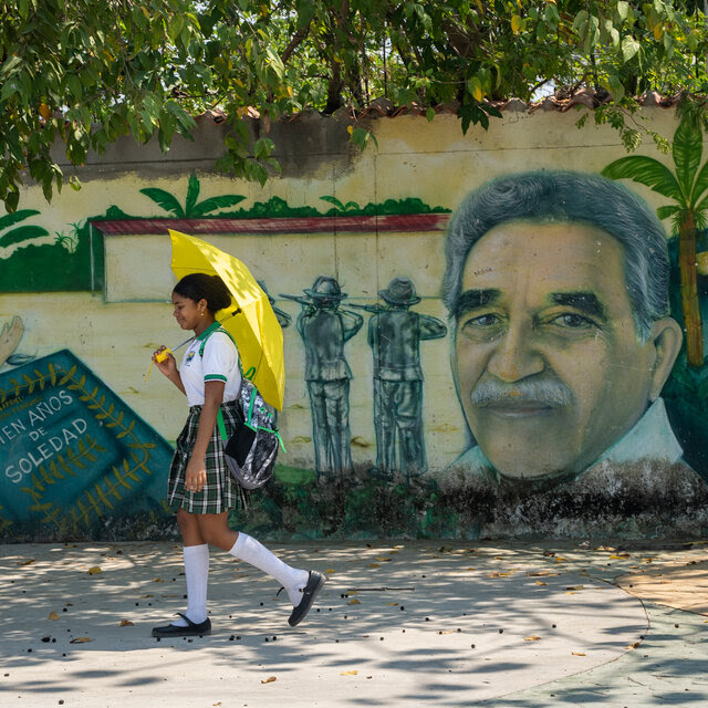 A girl walks with a yellow umbrella past a mural showing author Gabriel García Márquez.