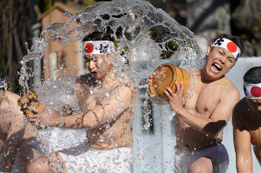 Shrine parishioners throw cold water on themselves. They are shirtless and look startled by the cold water.