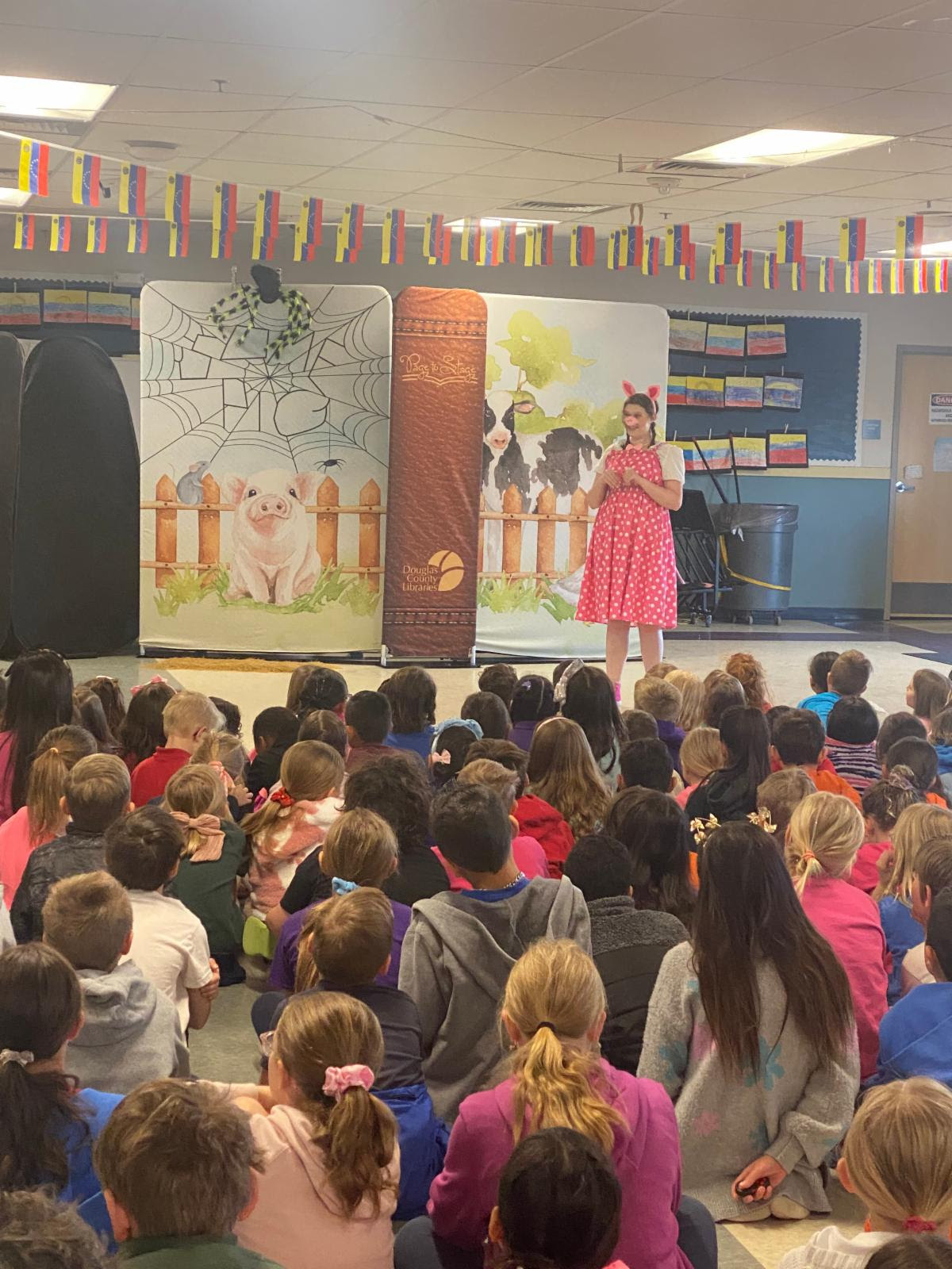 students watching actors perform a play with a spider web and farm scene backdrop