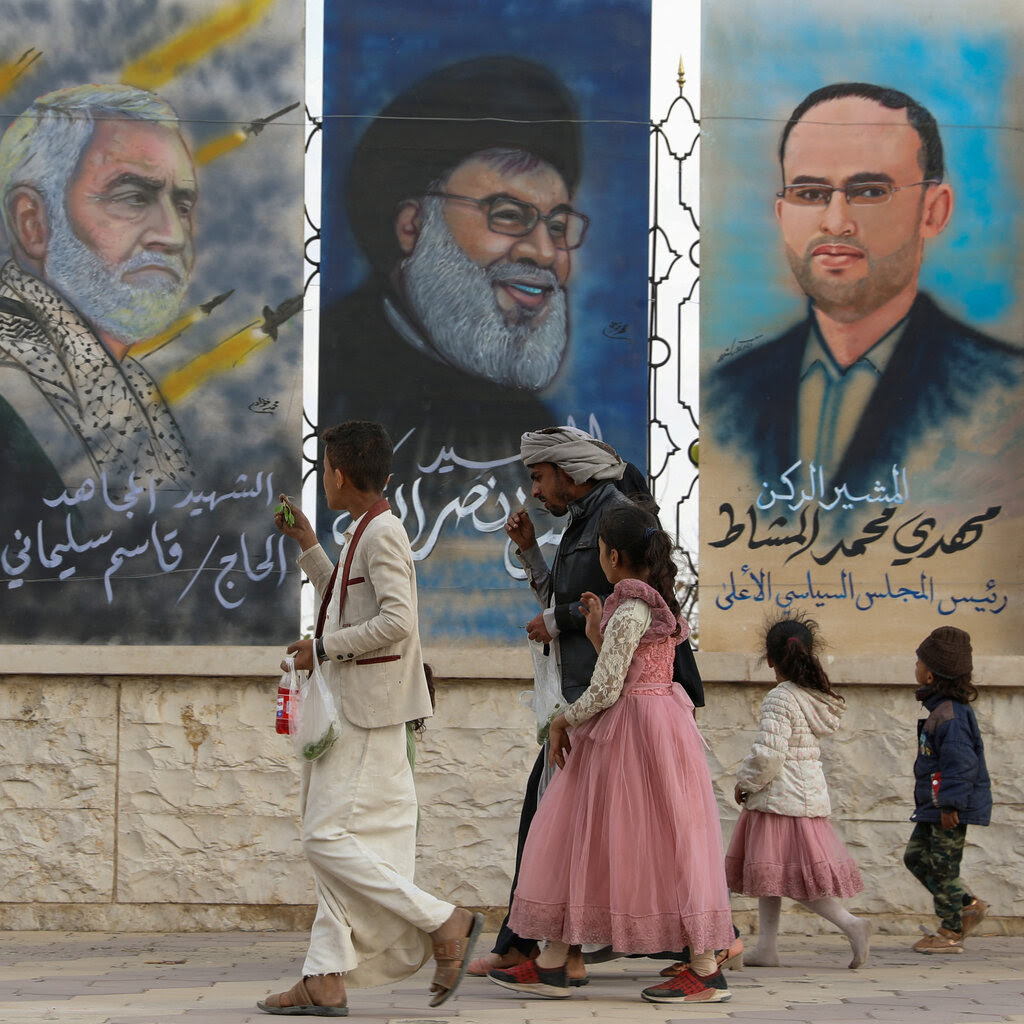 People walk past posters of men with arabic writing below.