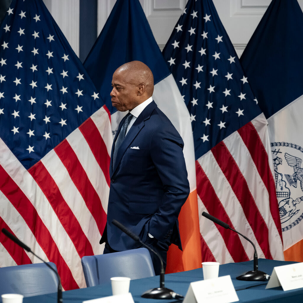 Mayor Eric Adams stands in front of a row of flags.