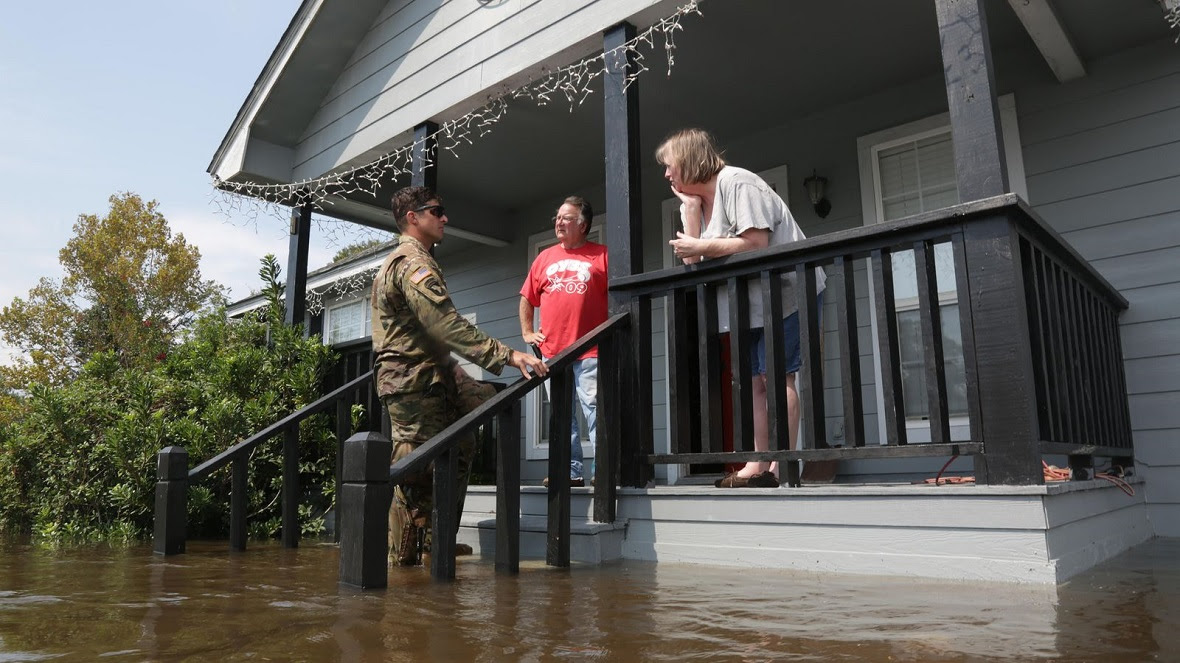 A military officer standing in flood water speaks to residents outside their home in Texas after Hurricane Harvey (Credit: Alamy)