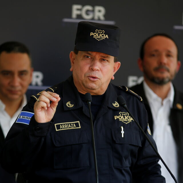 A man in a police uniform speaks with two men standing behind him.