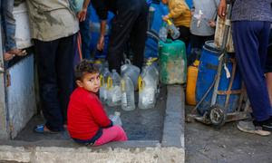 Un niño sentado junto a un punto de agua en Gaza.