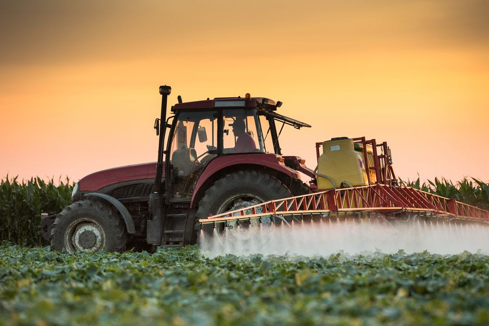 Un imposant tracteur pulvérisant des pesticides dans un champ de légumes.