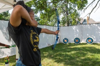 A young person draws back a mechanical bow, aiming for a distant target with sharp focus.