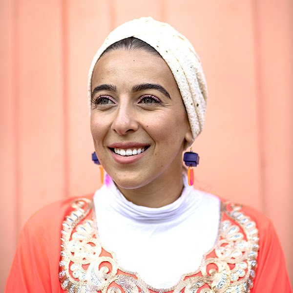 A woman standing in front of an orange wall, smiling to the left of the camera