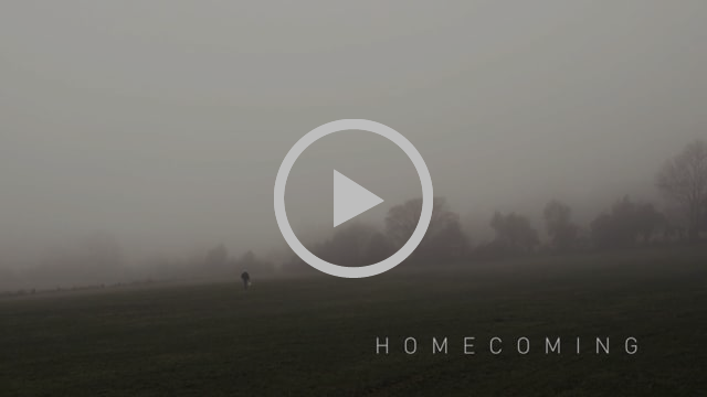 A misty field with a man walking in the distance and the title of the short film, 'Homecoming', in the bottom right-hand corner. There is also a play button to watch the film