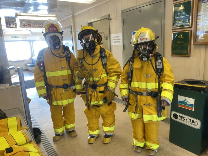 Three youth wearing firefighting gear in the passenger cabin of a ferry