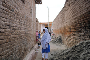 A girl is glancing back as she is walking between two brick buildings. There are more girls in the distance.