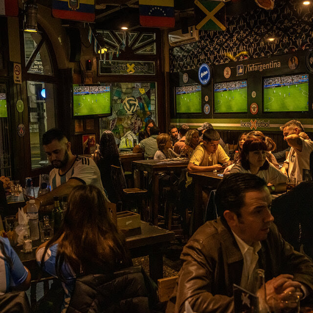 People sitting at tables inside a restaurant as televisions broadcast a soccer match.