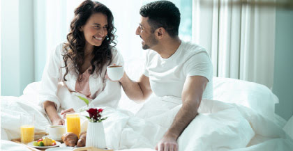 A woman and man smiling at each other enjoy breakfast in bed at an Atlantic City resort.