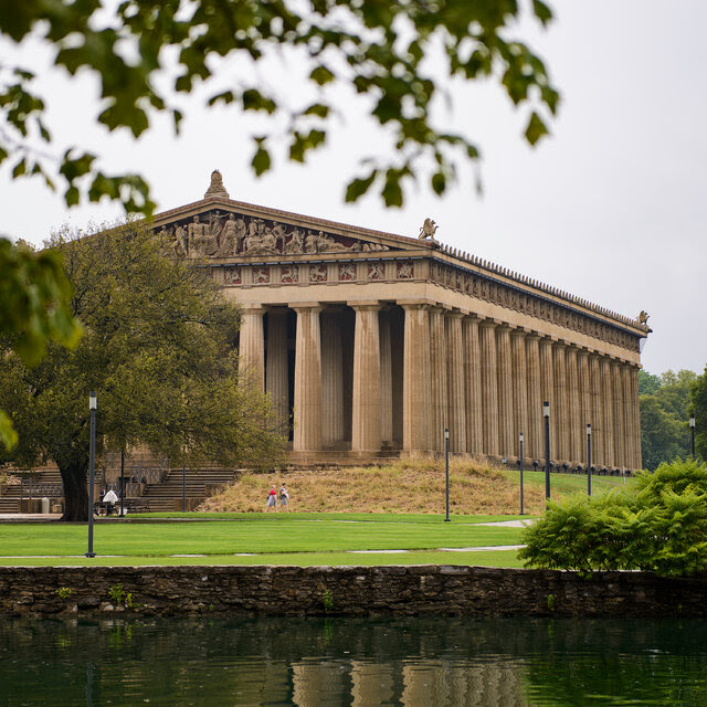 A photograph of the Parthenon museum in Nashville, with its front columns partially obscured by trees. 