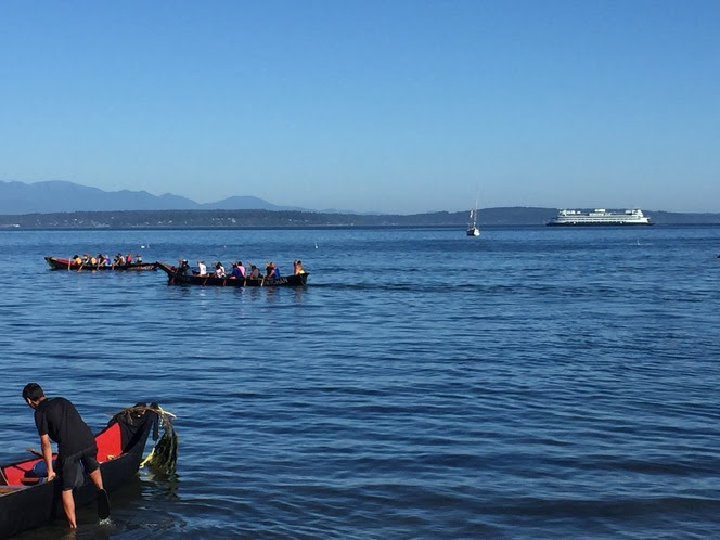 Tribal canoes in water with a ferry in the background