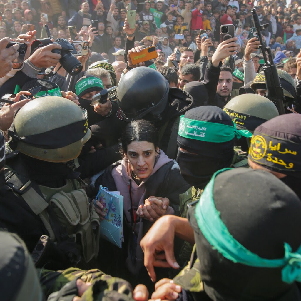 A large crowd surrounding a person. People in military helmets and face masks move the person through the crowd.