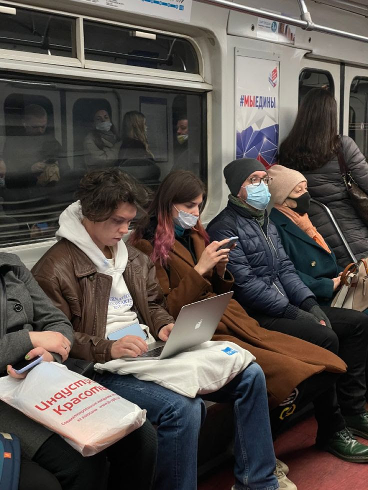 This may contain: people sitting on a subway train wearing masks and using their laptops to check the time