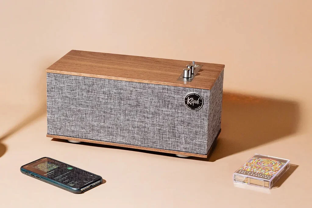 A mobile phone, a speaker and a cassette tape sit on a beige background.