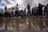 a group of mostly men and young boys walk around on wet ground