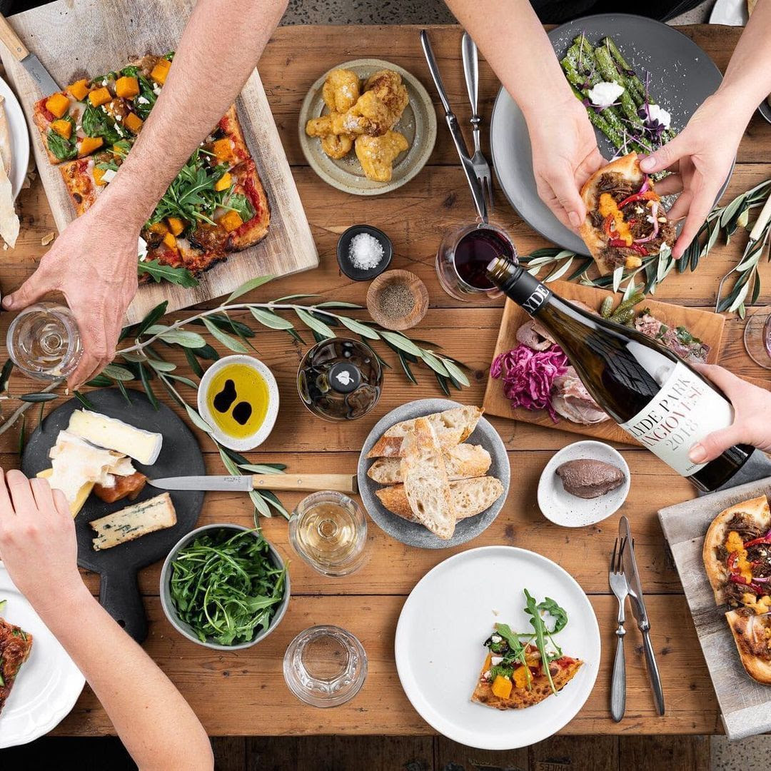 a group of people sitting around a table eating food and drinking wine