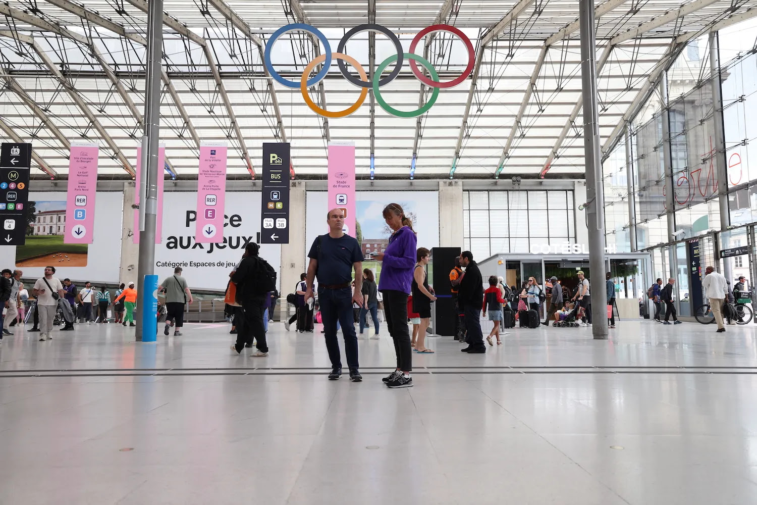 People wait under the Olympic Rings at a Paris train station.