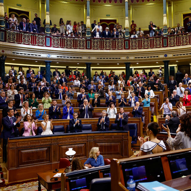 People stand in Spain’s Parliament, several of them clapping.