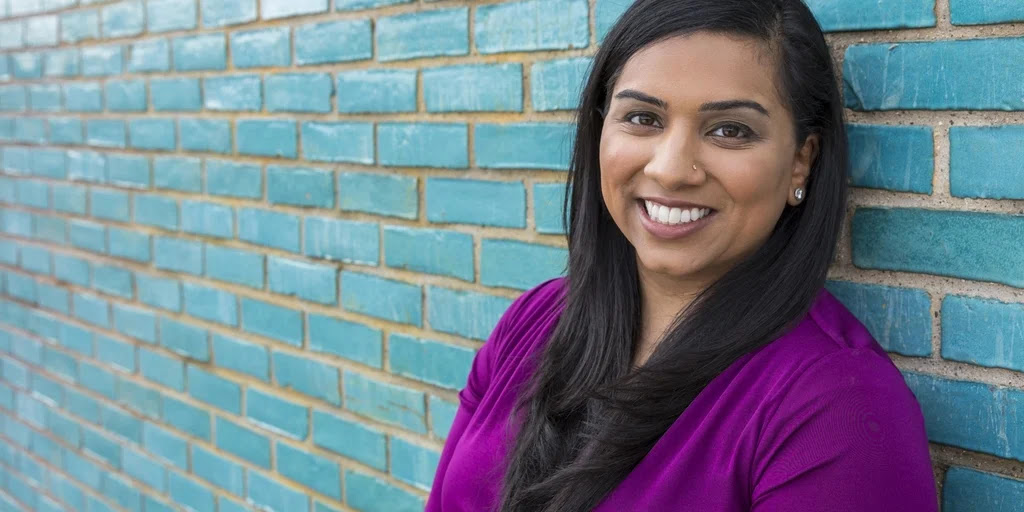 Smiling WOC with a red shirt, black jacket and red lipstick