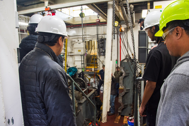 4 people with hard hats looking at a ferry's engine room