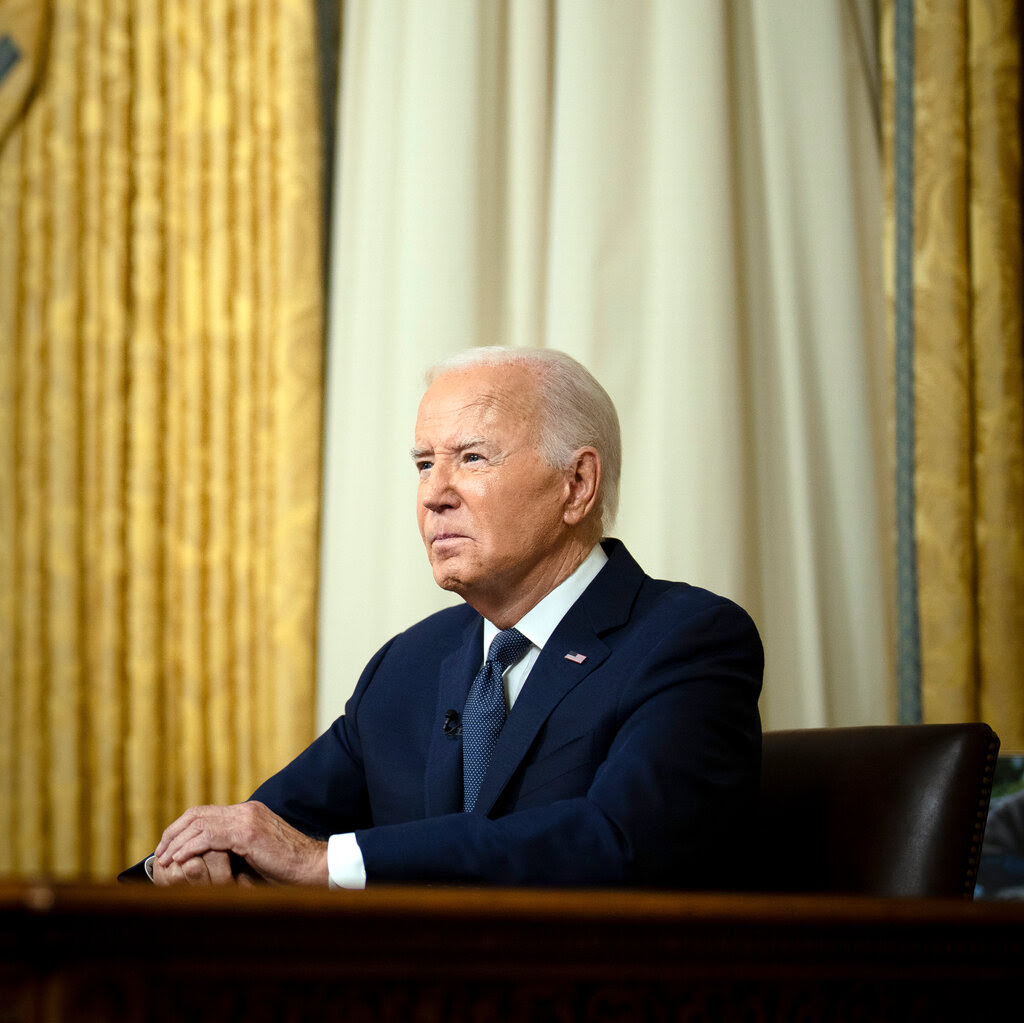 President Biden sits and looks ahead, viewed slightly in profile, as he delivers an address from the Oval Office.