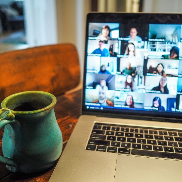 Close-up of a mug next to a laptop with a screen showing many people in boxes for an online video meeting