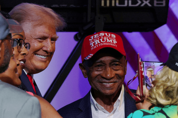 Man getting a photo takes of him and trump with a hat saying 