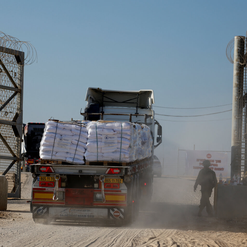 A truck with pallets of aid supplies drives by a tall gate topped with barbed wire.