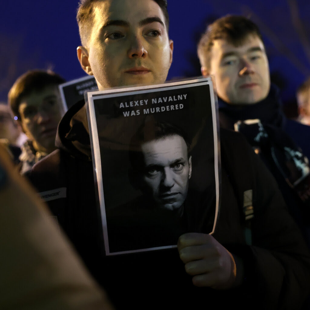 A person in a crowd holds a sign with a picture of Aleksei A. Navalny and the text “Alexey Navalny Was Murdered.”