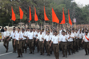 A group of men in white shirts are carrying orange flags and marching through the street.