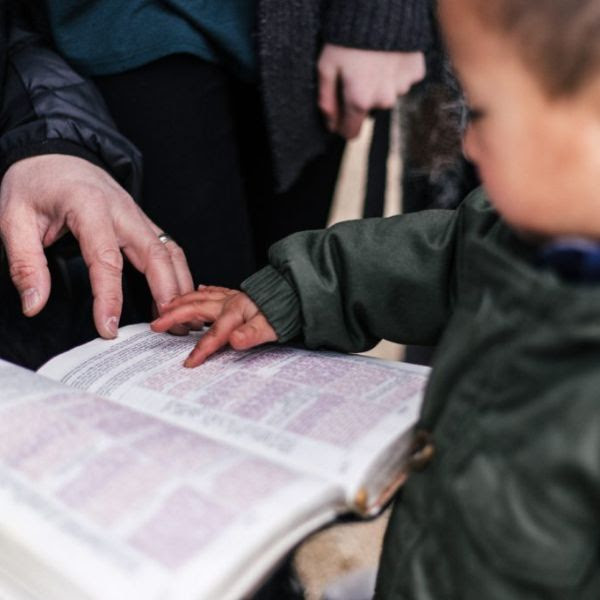 A close-up side view of a child touching an open book with their finger