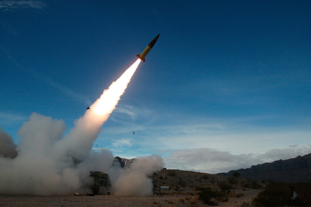 A missile is launched from the ground with a fiery trail across a blue sky.