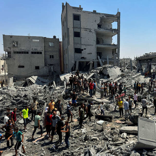 A crowd of people walking in the debris of destroyed buildings.