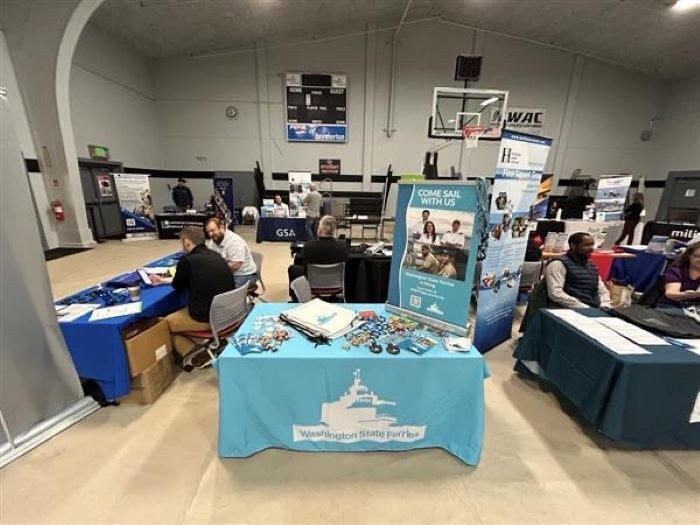 Indoor informational fair with tables and banners from various organizations, including Washington State Ferries