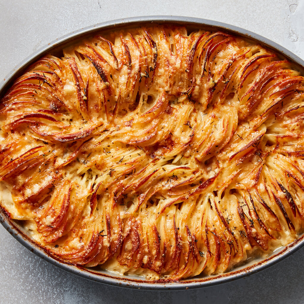 An overhead shot of cheesy Hasselback potato gratin shows packed, ruffly potatoes in a coat of browned, melted cheese.