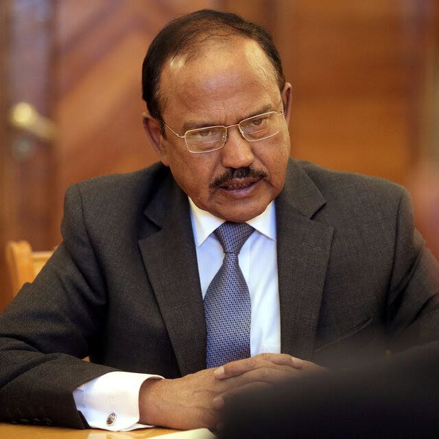 A man with a mustache and glasses in a suit seated at a table.