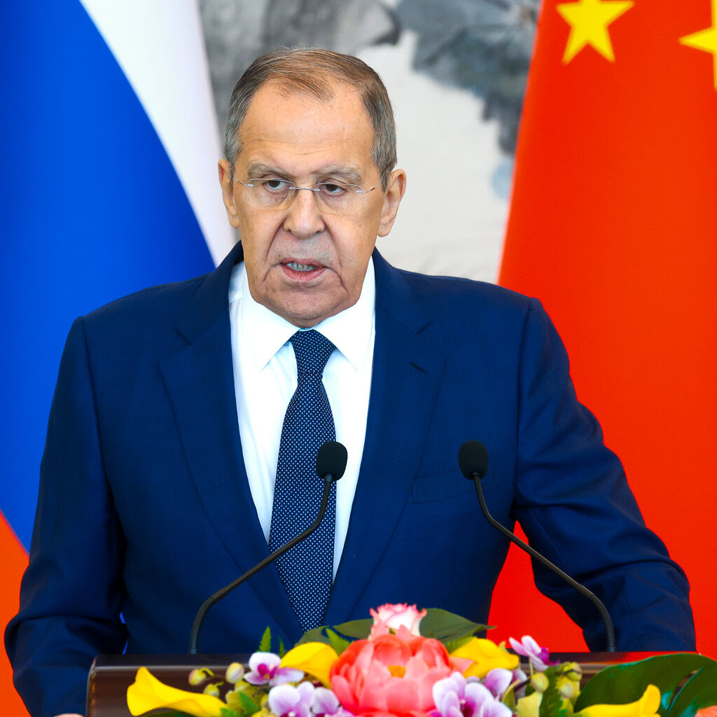 Sergey Lavrov speaking at a lectern with flowers in front of it.