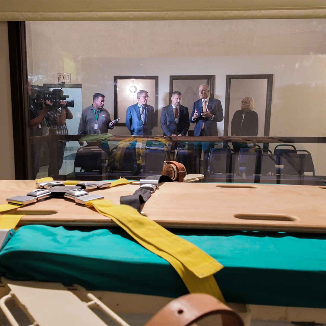 Group of people standing behind now-closed execution chamber glass wall. 